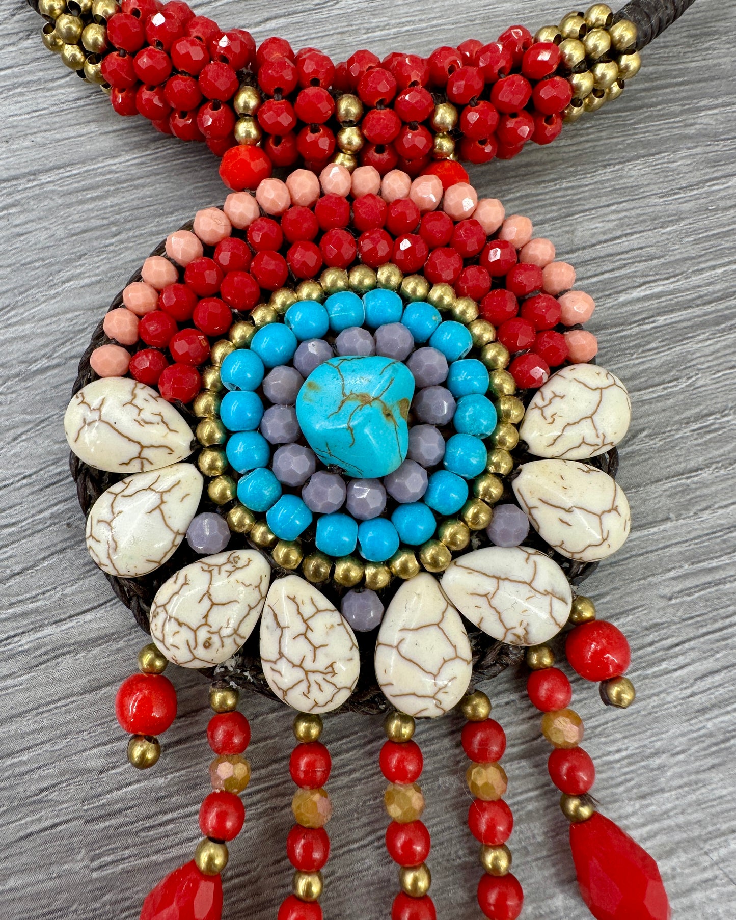 Dettaglio collana boho artigianale con pendente circolare decorato da turchese centrale, pietre naturali rosse e dettagli color avorio