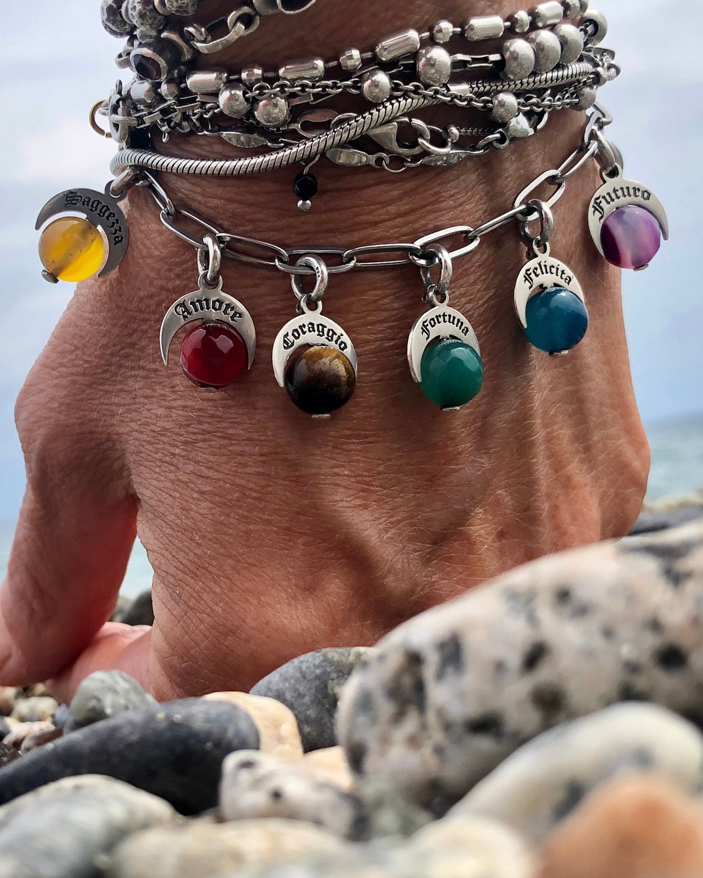 Bracciale Talismani Naja in argento 925 con charms simbolici e pietre naturali colorate, indossato al polso vicino al mare.