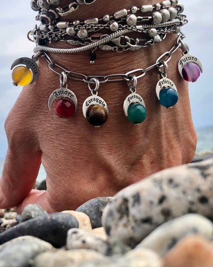 Bracciale Talismani Naja in argento 925 con charms simbolici e pietre naturali colorate, indossato al polso vicino al mare.