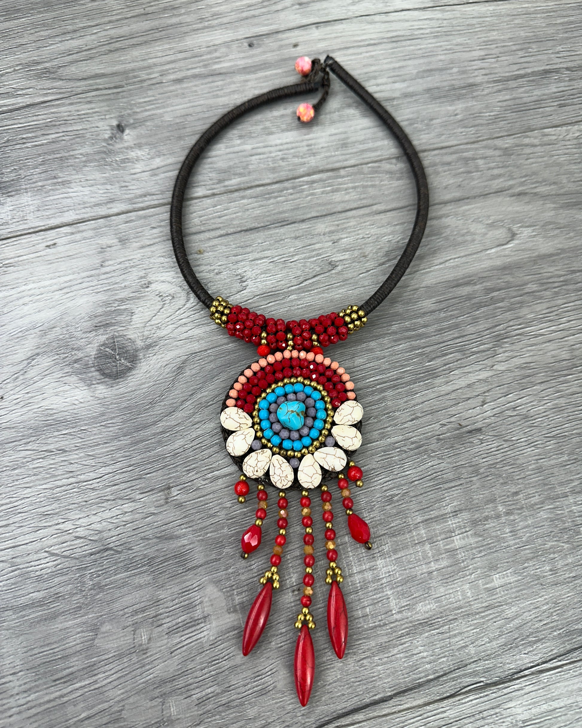 Collana boho artigianale con pendente circolare decorato da turchese centrale, pietre naturali rosse e dettagli color avorio su cordoncino regolabile.