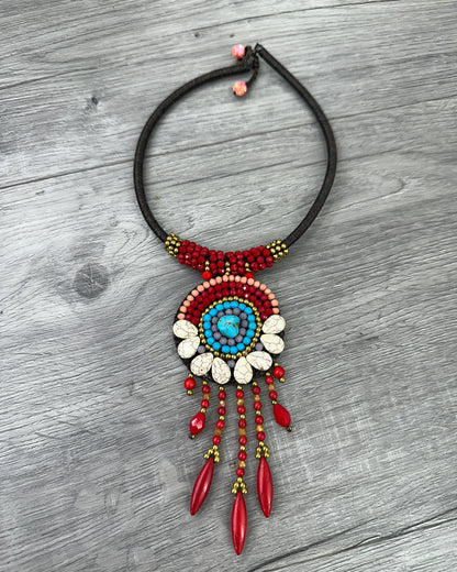 Collana boho artigianale con pendente circolare decorato da turchese centrale, pietre naturali rosse e dettagli color avorio su cordoncino regolabile.