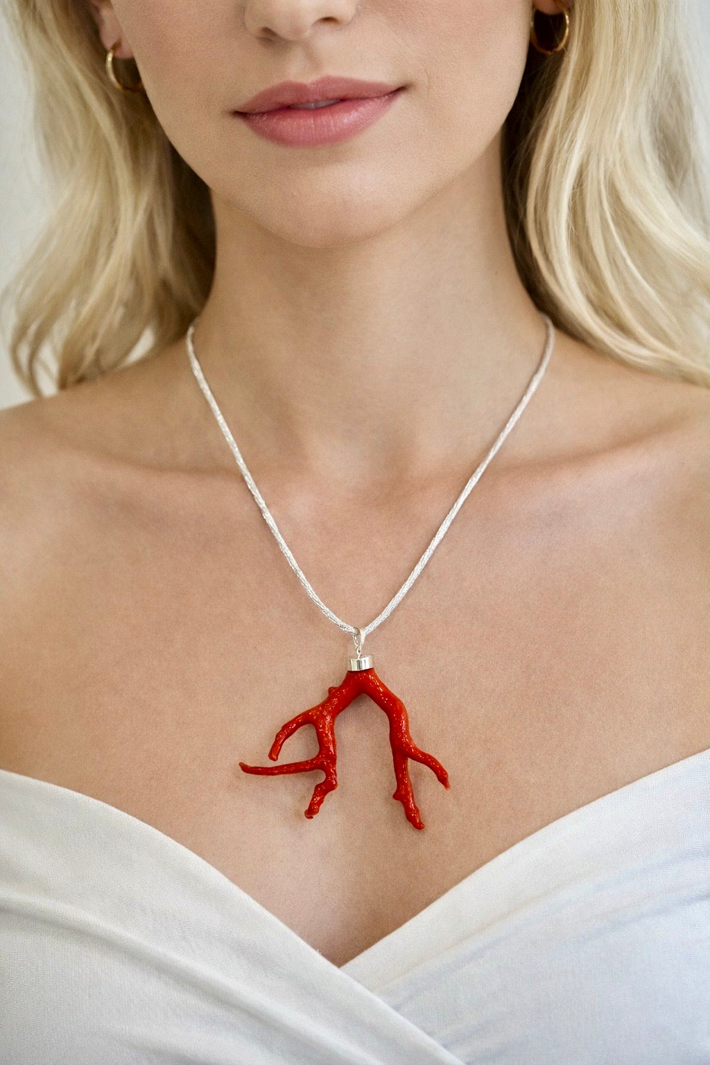 Collana con pendente in corallo rosso naturale su cordino chiaro in seta indossata su décolleté femminile.
