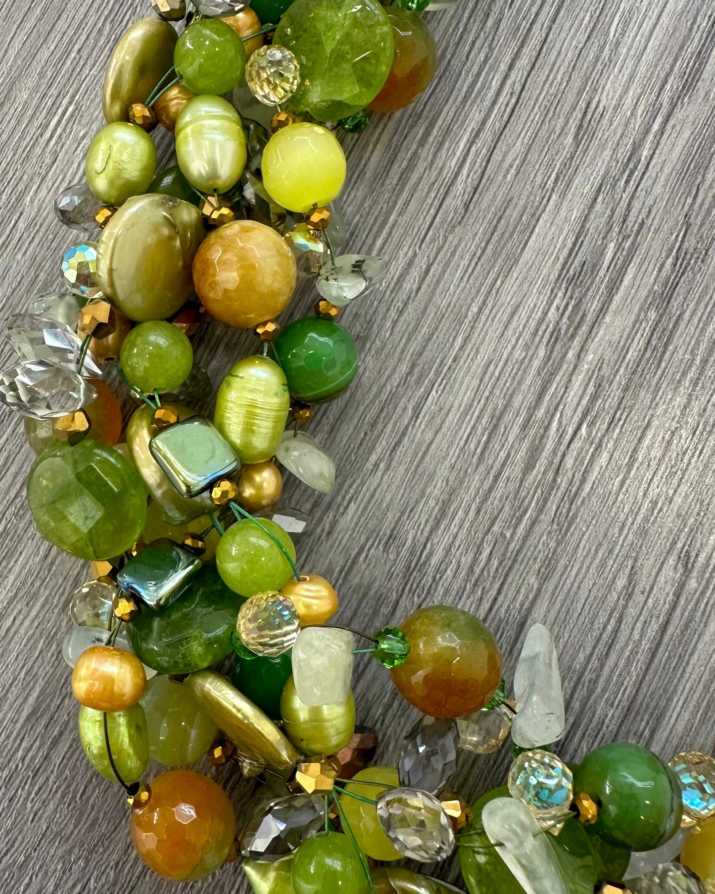 Dettaglio collana intrecciata artigianale con pietre naturali verdi, perle luminose e cristalli sfaccettati￼