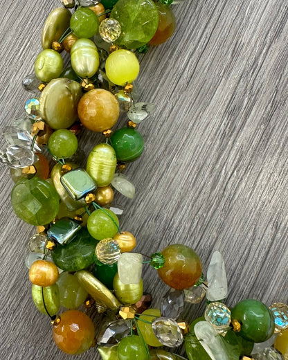Dettaglio collana intrecciata artigianale con pietre naturali verdi, perle luminose e cristalli sfaccettati￼