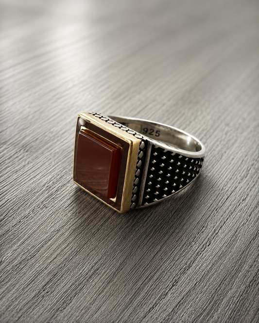 Anello chevalier geometrico in argento 925 con pietra naturale corniola color rosso intenso e dettagli bruniti laterali, in stile minimal su superficie grigio effetto legno.