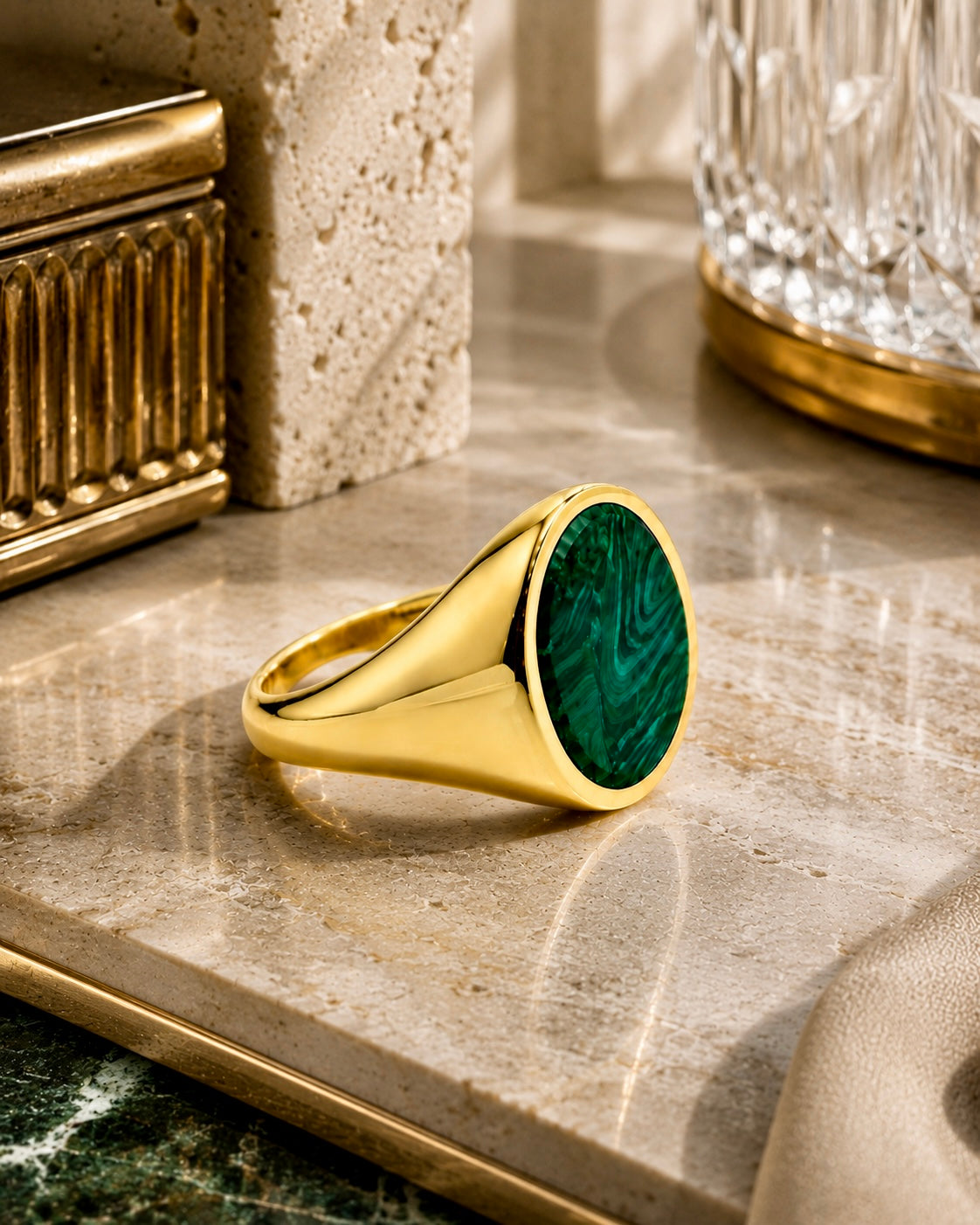 Anello chevalier in argento dorato con pietra verde effetto malachite su ambientazione neutra luxury beige e marmo, fotografia editoriale elegante