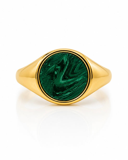 Anello chevalier in argento dorato con pietra verde effetto malachite indossato su mano femminile con manicure nera.