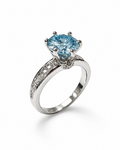 Anello in argento 925 con moissanite color acquamarina taglio brillante e pavé laterale, fotografato su sfondo bianco.