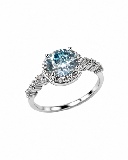 Anello in argento 925 con moissanite color acquamarina taglio brillante, contorno di moissaniti e fascia con dettagli pavé, fotografato su sfondo bianco.
