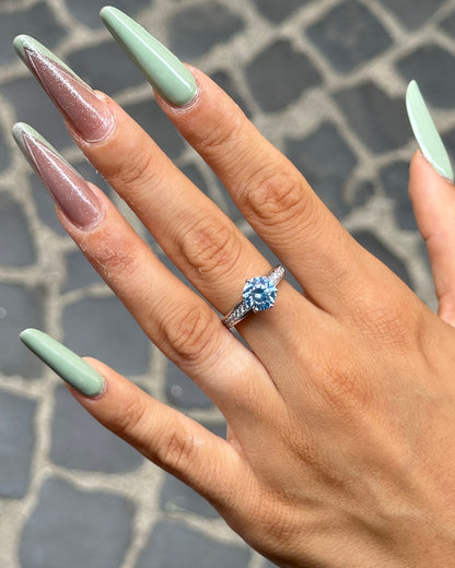 Anello solitario in Argento 925 con moissanite color acquamarina indossato sulla mano, dettaglio della pietra brillante e del pavé laterale.