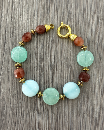 Bracciale aperto in argento dorato con Tormalina, Giada Verde e Azzurra ed Ematite dorata, con chiusura tonda visibile su legno grigio.