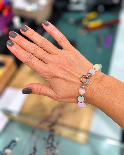 Bracciale in Argento, Ematite e Selenite nei colori pastello, indossato al polso con chiusura rotonda in vista e sfondo sfocato.
