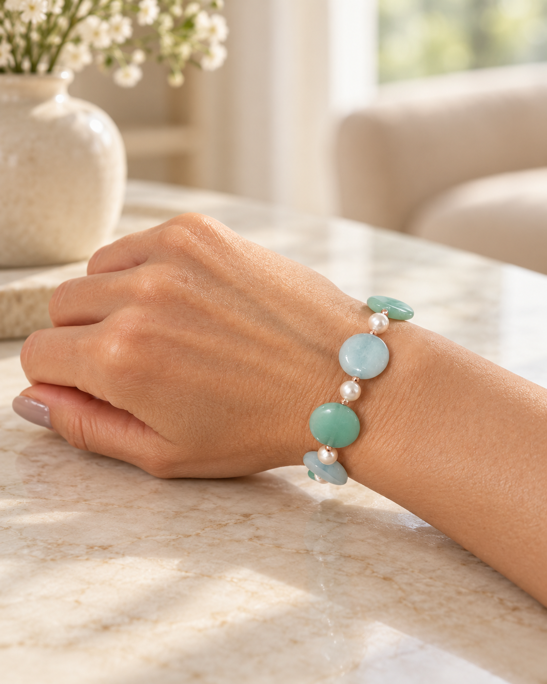 Bracciale in argento rosato con perle Maiorca e giada verde e azzurra, indossato al polso su un tavolo in marmo chiaro.
