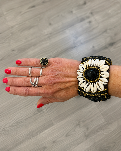 Bracciale boho con conchiglie naturali e pietra nera indossato al polso, stile etnico estivo.