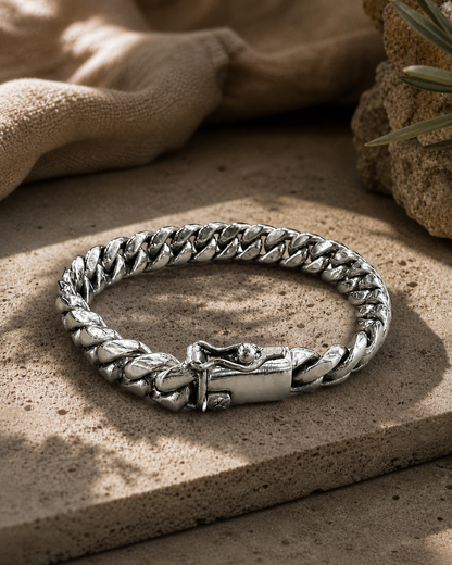 Bracciale Cuban Link uomo in Argento 925 ambientato su superficie effetto pietra con luce calda naturale e stile luxury contemporaneo.