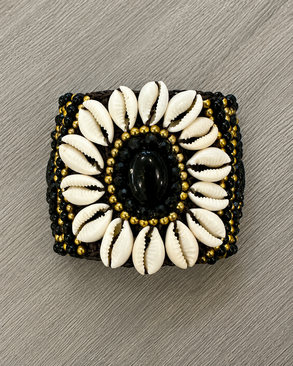Bracciale boho artigianale con conchiglie naturali, perline nere e dettagli dorati con pietra nera centrale.