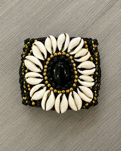 Bracciale boho artigianale con conchiglie naturali, perline nere e dettagli dorati con pietra nera centrale.