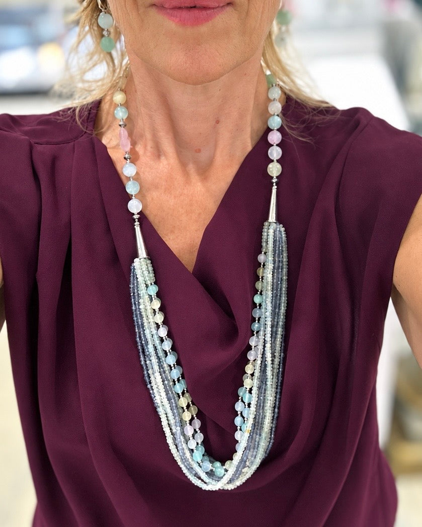 Collana lunga multifilo in Acquamarina, Radice di Zaffiro e Selenite nei colori pastello, indossata su abito bordeaux con sfondo sfocato.