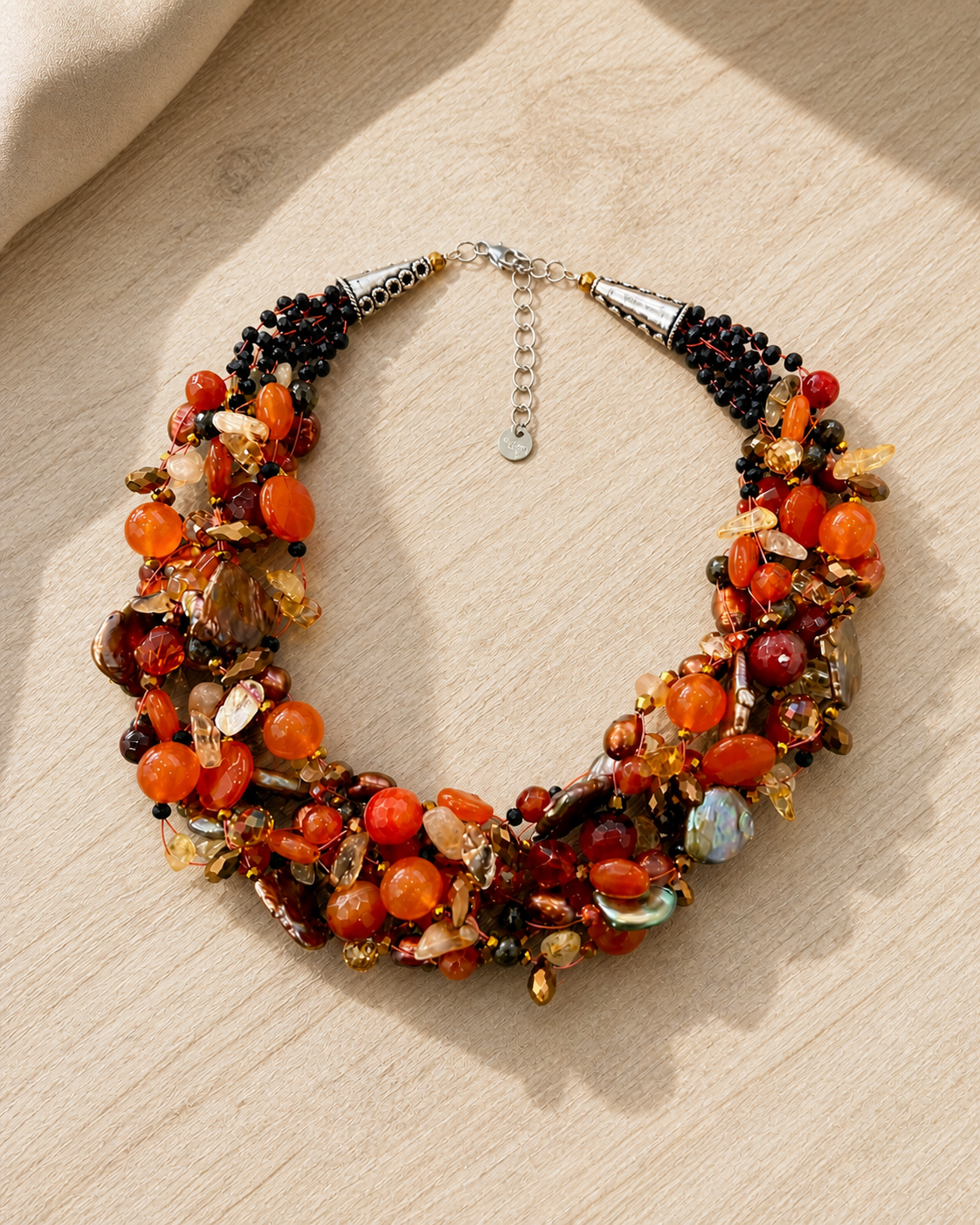 Collana artigianale arancio multifilo con pietre naturali e perle su fondo legno chiaro, stile elegante Attimi Gioielli