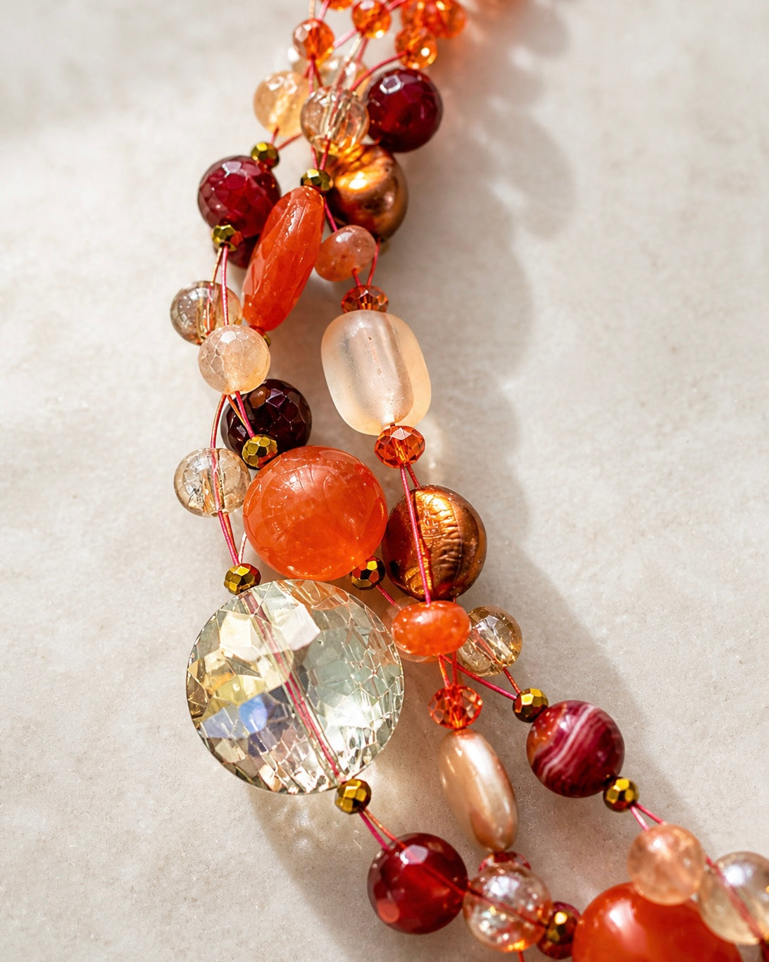 Dettaglio collana artigianale intrecciata con pietre naturali, perle e cristalli nei toni arancio, lavorazione fatta a mano