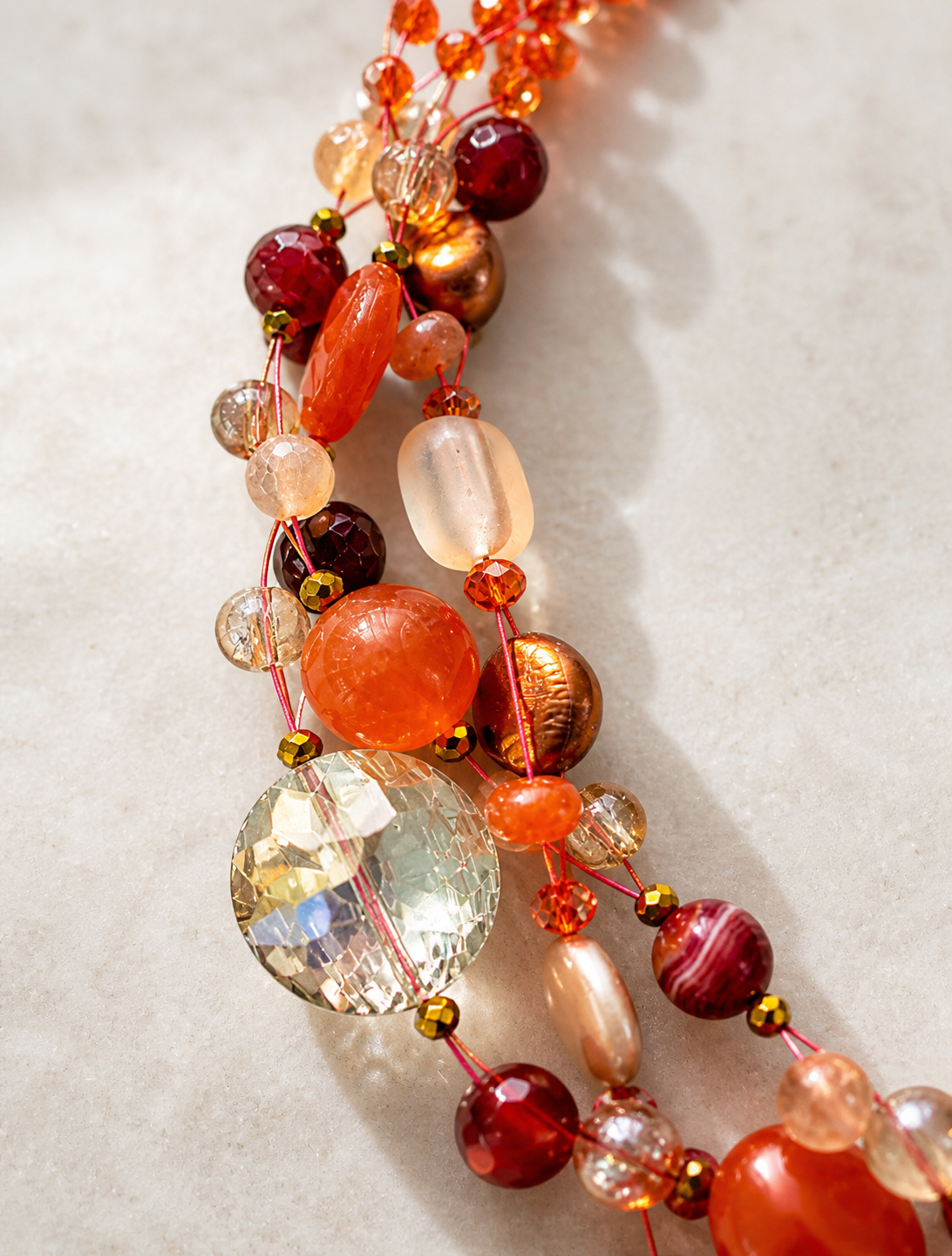 Dettaglio collana artigianale intrecciata con pietre naturali, perle e cristalli nei toni arancio, lavorazione fatta a mano