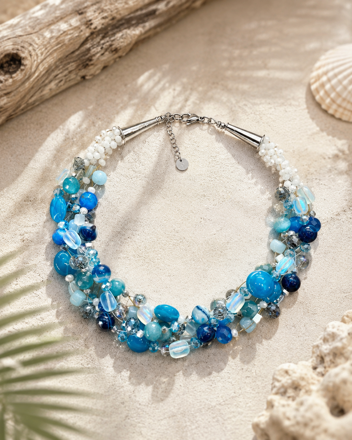     Dettaglio collana multifilo artigianale con cristalli luminosi, pietre naturali blu oceano e perline bianche intrecciate.
