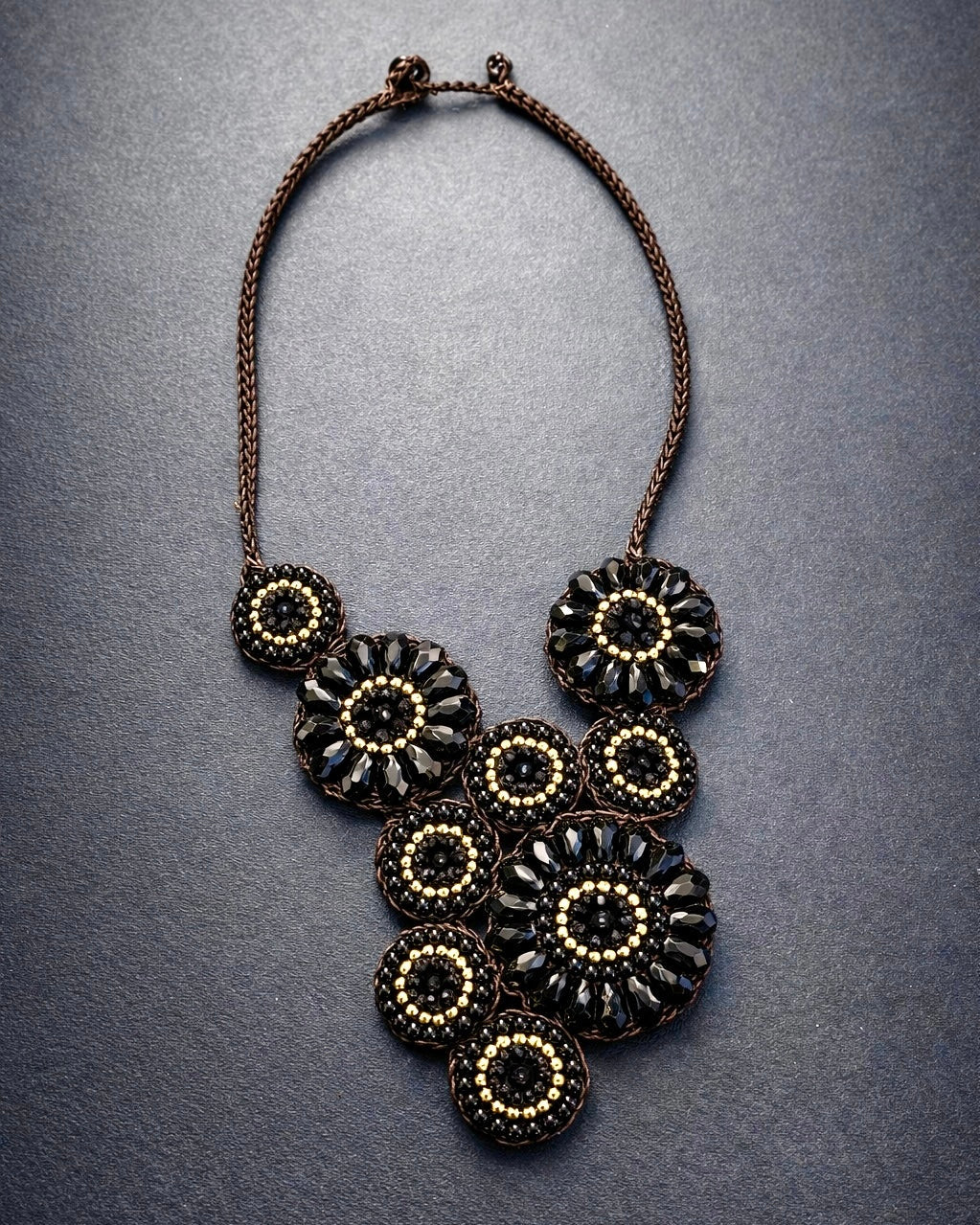 Collana artigianale nero e oro con motivo floreale in cristallo, design elegante su base intrecciata marrone