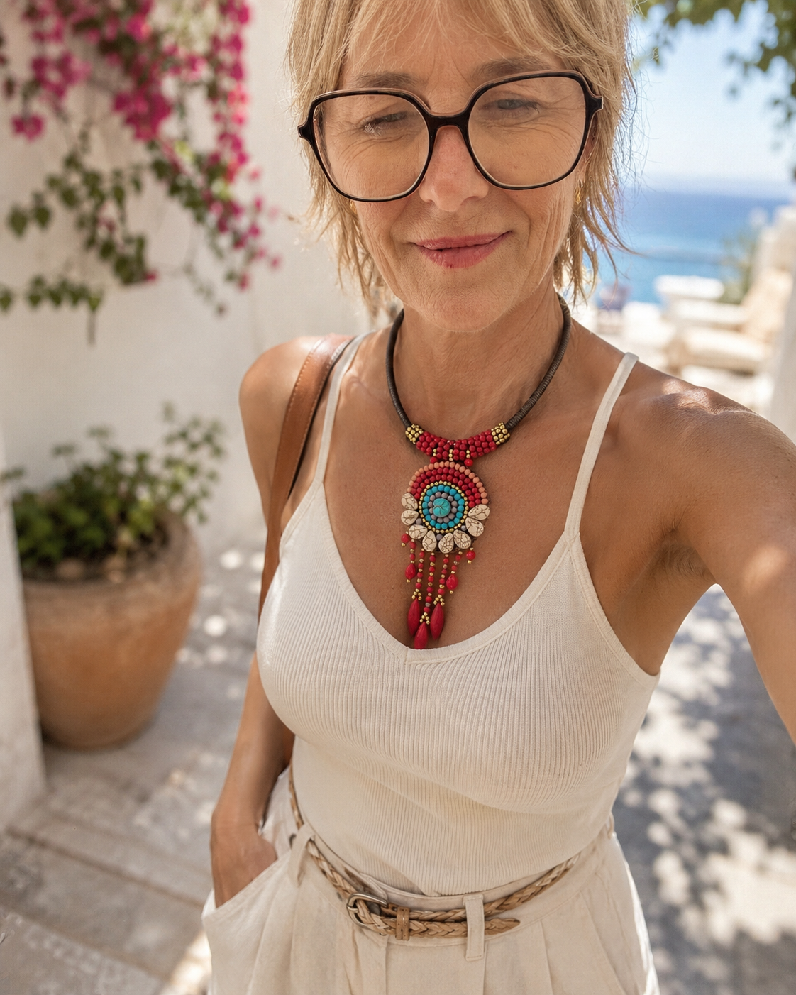 Collana boho etnica con perline rosse, turchesi e dettagli pendenti indossata da una giovane modella con outfit estivo chiaro in ambientazione mediterranea luminosa.