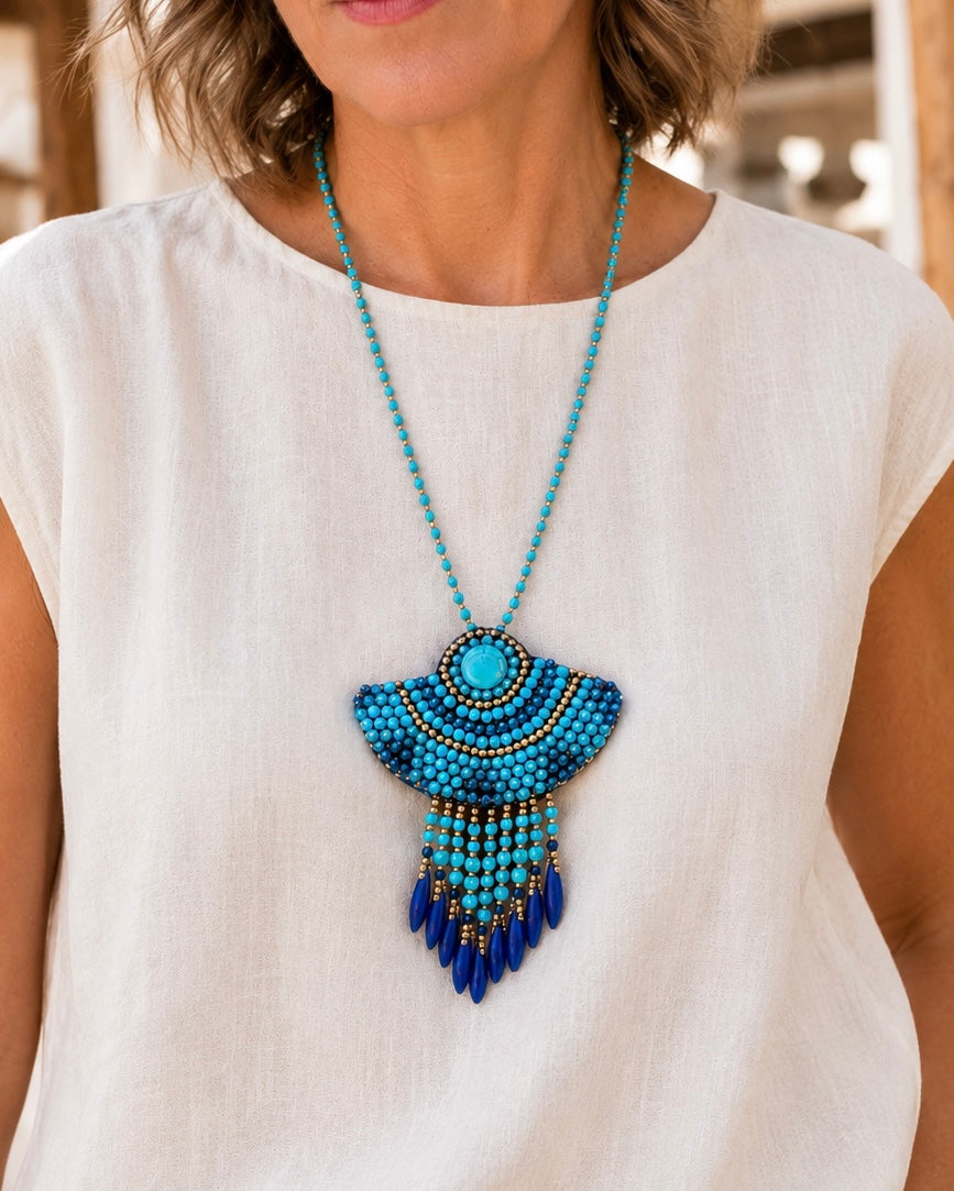 Modella con outfit estivo che indossa una collana boho turchese con grande ciondolo ricamato e pendenti blu.