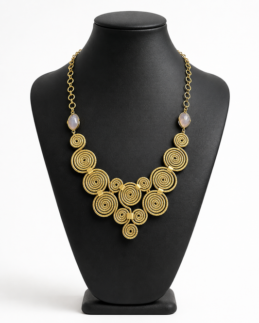Collana artigianale Capim Dourado con spirali dorate e pietra viola esposta su busto nero per catalogo Shopify.
