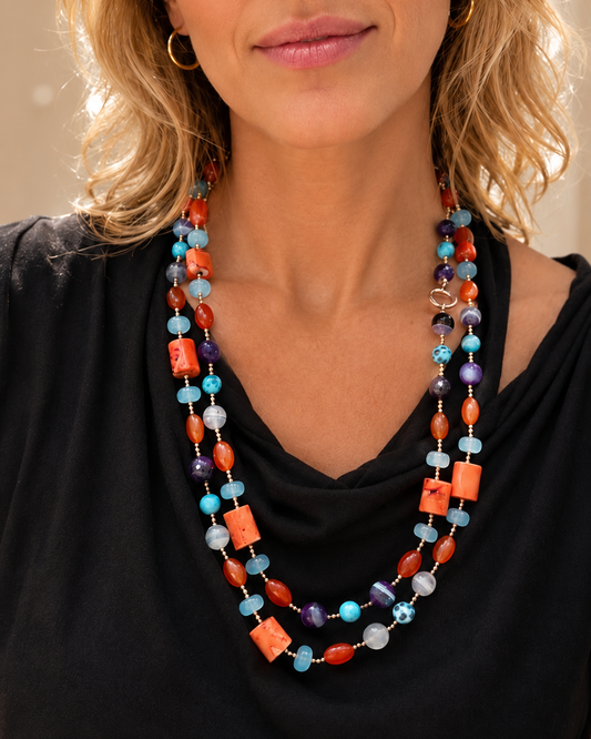 Collana artigianale con corallo bambù, agata azzurra, agata viola, corniola, perline turchesi, ematite rosata e dettagli in argento 925 dorato, indossata da modella.