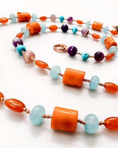 Collana artigianale con corallo bambù, giada azzurra, agata viola e dettagli in argento rosato, fotografata su busto bianco per catalogo.
