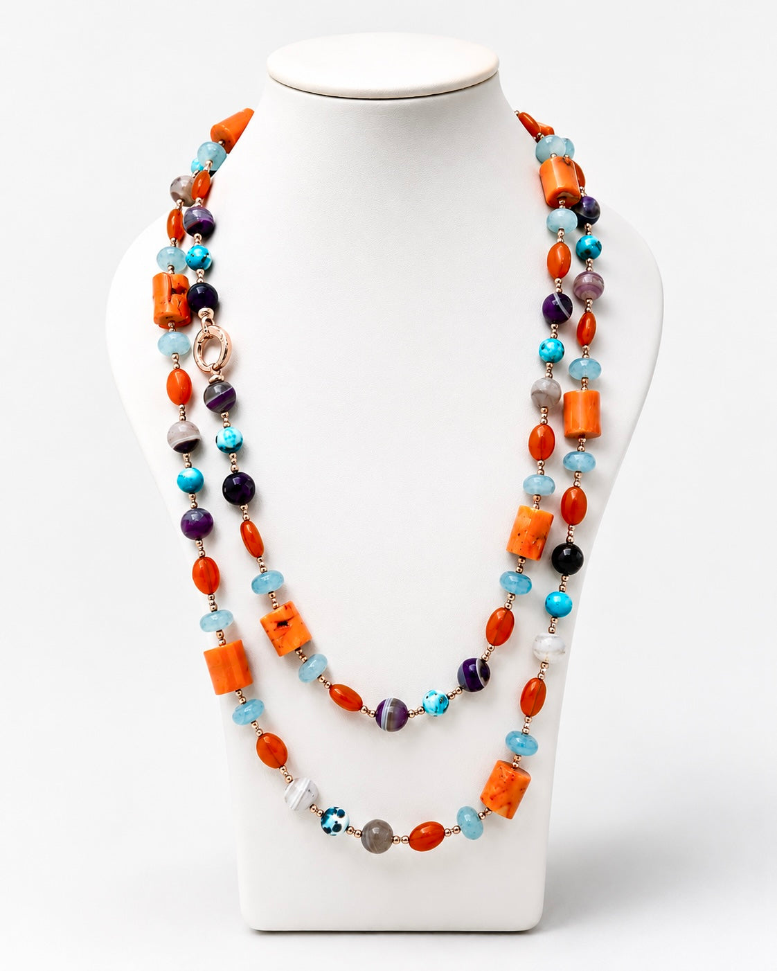 Collana lunga artigianale con corallo bambù, giada azzurra, agata viola e dettagli in argento rosato, fotografata su busto espositivo.