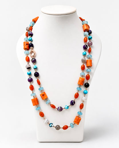 Collana lunga artigianale con corallo bambù, giada azzurra, agata viola e dettagli in argento rosato, fotografata su busto espositivo.