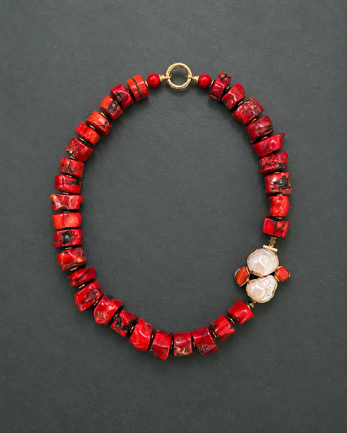 Collana artigianale in corallo bambù rosso, perle barocche naturali ed ematite dorata su fondo neutro.
