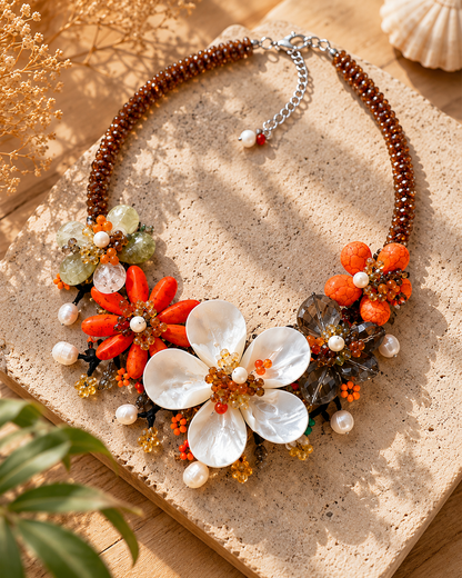 Collana floreale nei toni arancio, ambra e madreperla, fotografata in ambientazione naturale elegante e luminosa.