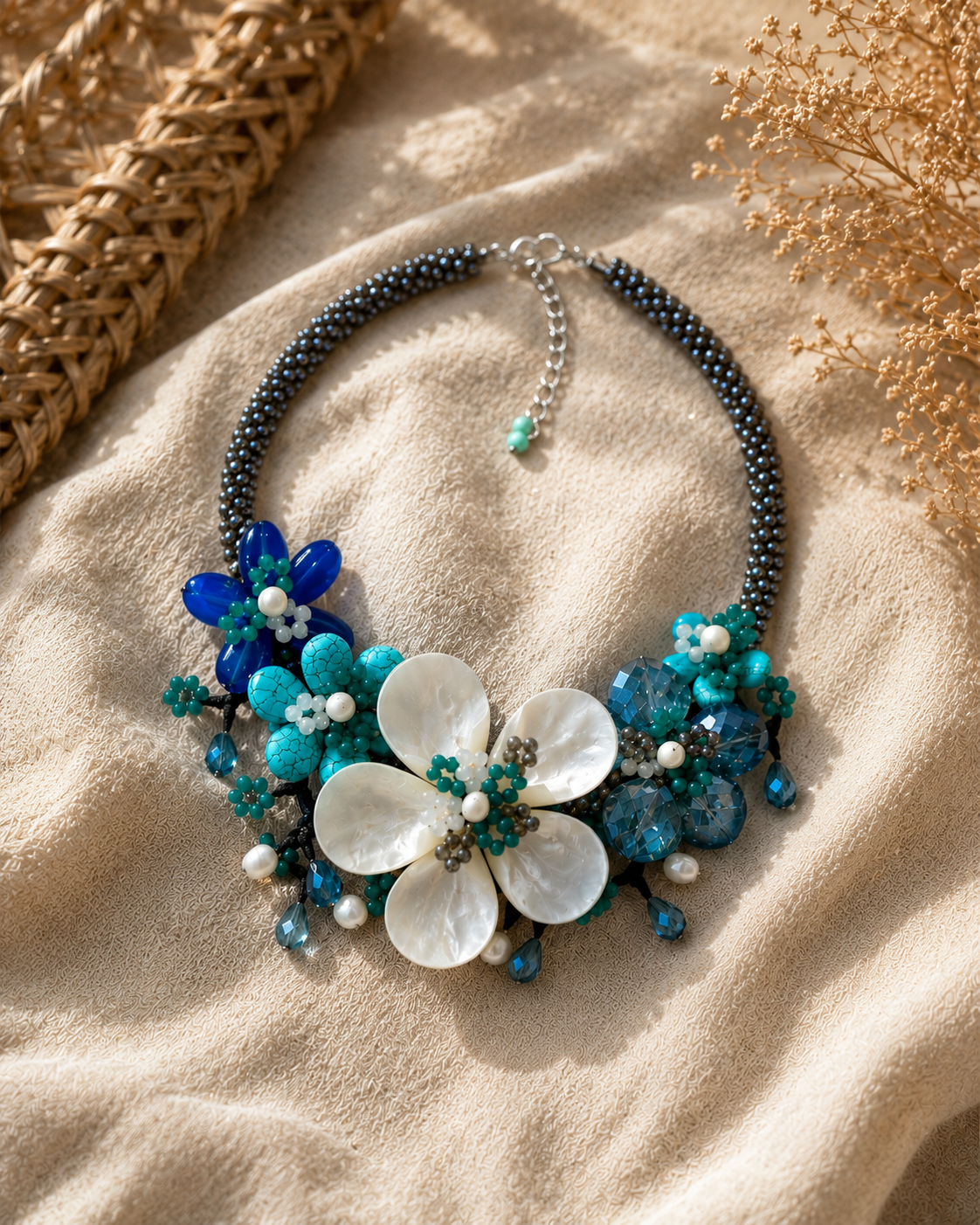 Collana floreale nei toni del turchese e del blu con madreperla e perle naturali, fotografata in ambientazione elegante dai colori neutri.
