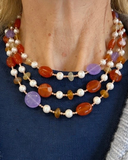     Modella che indossa una collana artigianale trasformabile a doppio giro con Giada viola, Giada arancio, Corniola, Perle ed Ematite rosata.