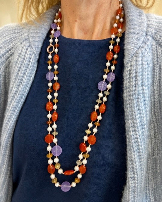     Modella che indossa una collana artigianale lunga con Giada viola, Giada arancio, Corniola, Perle ed Ematite rosata.