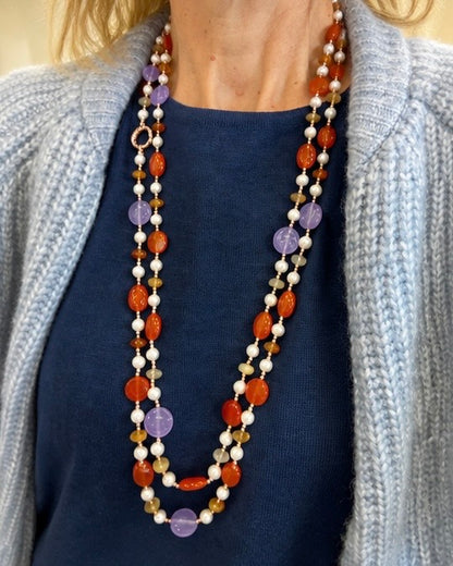     Modella che indossa una collana artigianale lunga con Giada viola, Giada arancio, Corniola, Perle ed Ematite rosata.