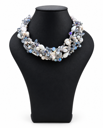 Collana intrecciata color ghiaccio con perle e cristalli luminosi nelle sfumature del bianco, azzurro ghiaccio e argento, su busto nero.