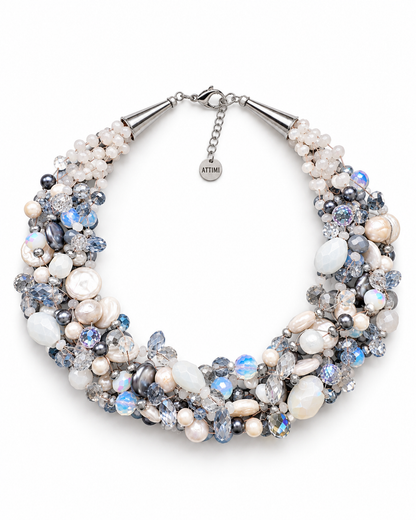Collana intrecciata color ghiaccio con perle e cristalli nelle sfumature del bianco, azzurro e argento, fotografata aperta su fondo bianco con chiusura regolabile e targhetta Attimi Gioielli.