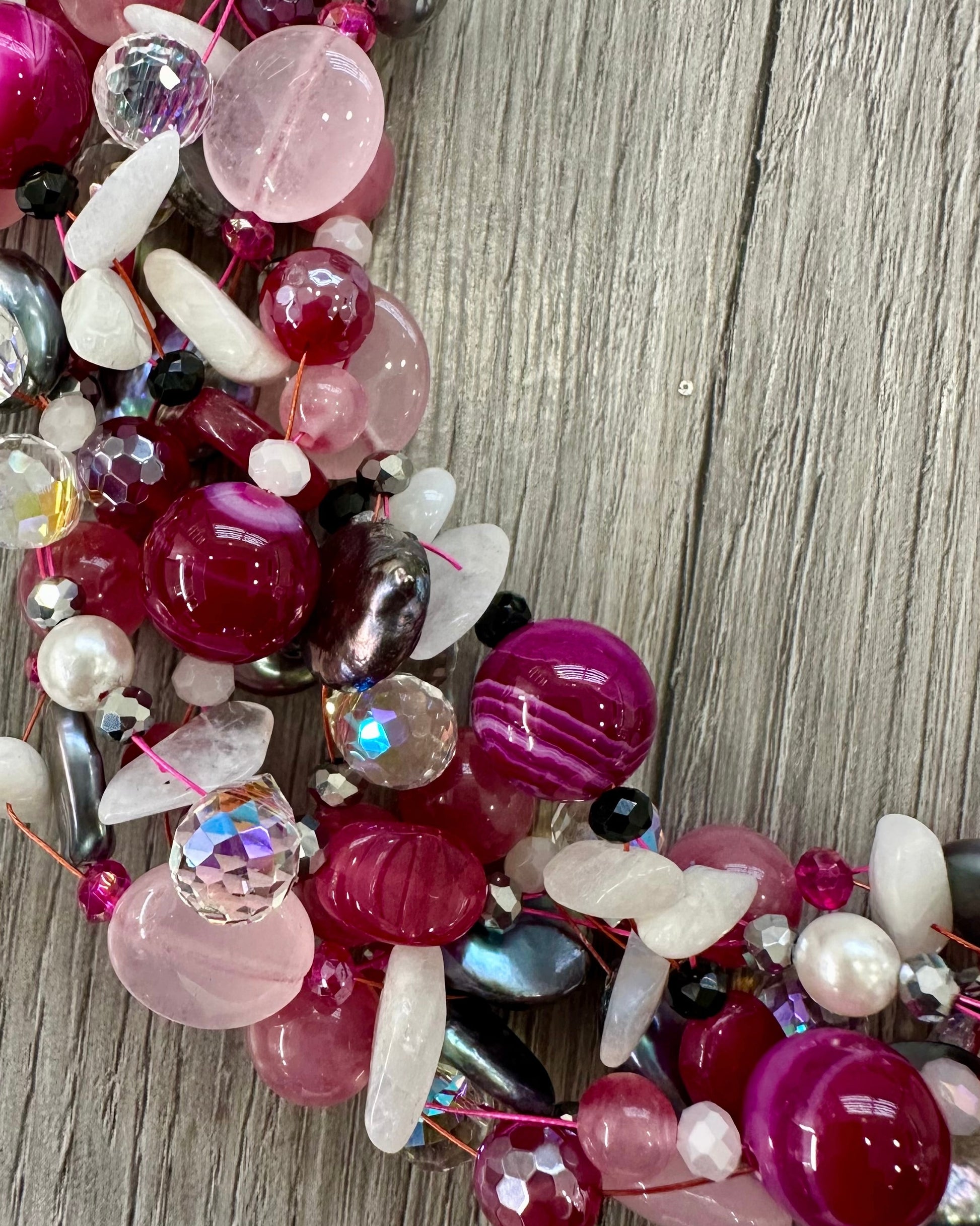 Dettaglio collana intrecciata con perle, pietre rosa fuxia e cristalli luminosi