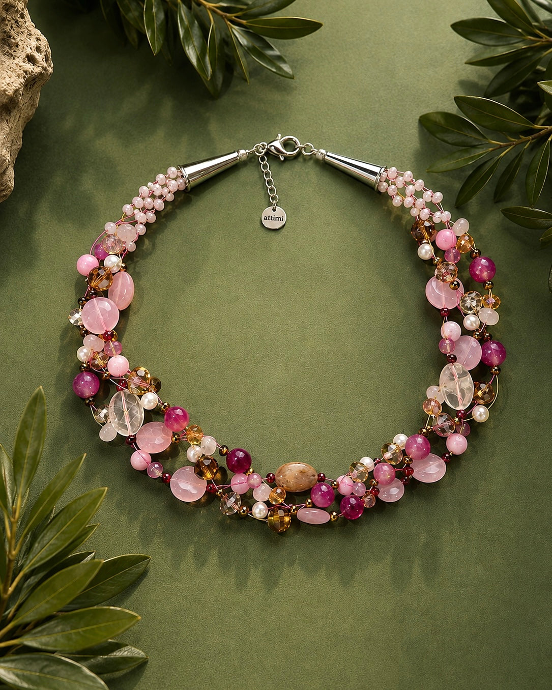Collana artigianale intrecciata con Quarzo Rosa e pietre color melograno in foto ambientata su fondo verde.