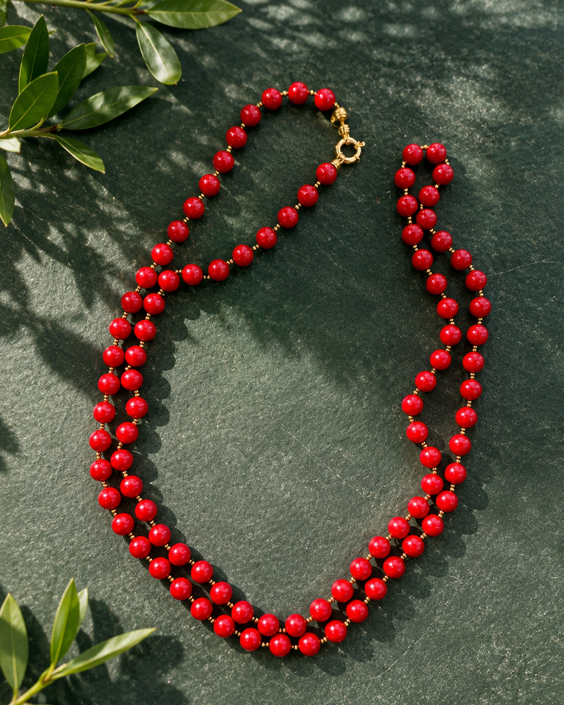 Collana lunga con Perle di Maiorca rosse ed ematite dorata fotografata su sfondo verde naturale.