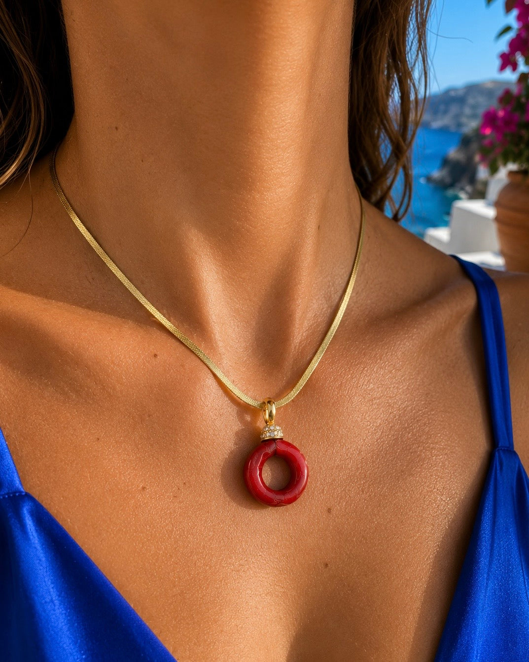 Collana con pendente in corallo rosso e catenina snake in argento 925 dorato, indossata con abito blu elettrico in stile mediterraneo