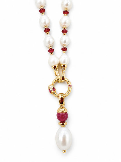 Collana con perle barocche bianche, dettagli rossi e pendente serpente dorato con pietra ruby e perla pendente su sfondo bianco.