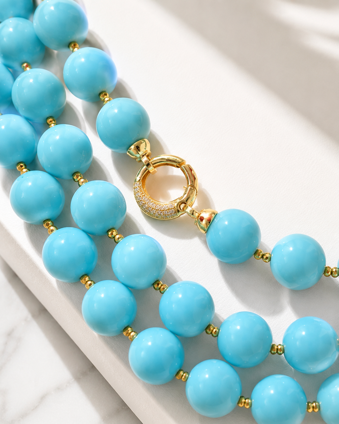 Dettaglio della chiusura a moschettone in Argento 925 dorato con zirconi bianchi su collana artigianale in pasta di turchese ed ematite dorata.