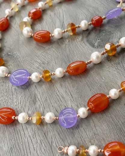     Dettaglio della collana artigianale con Giada viola, Giada arancio, Corniola, Perle ed Ematite rosata, con particolare delle pietre naturali e della lavorazione.