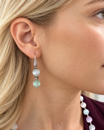 Primo piano di un orecchino pendente in Argento 925 con sfere di Selenite azzurro chiaro e verde acqua, indossato da una modella.
